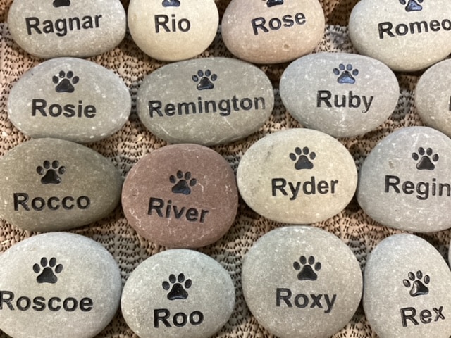 Many engraved rocks that have a paw print graphic with various pet names