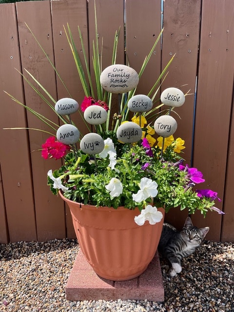 A potted plant with rod mounted engraved rocks sticking out of the plant that have various name from the family.