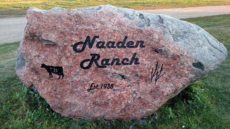 Large red Engraved stone that says Naaden Ranch, with custom cow engraving.