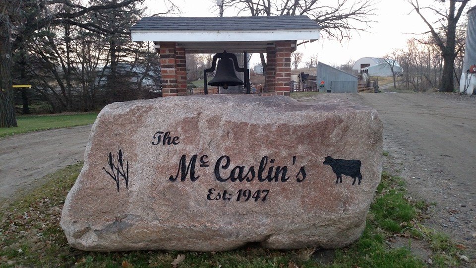 Large brown engraved rock that says The McCaslin's, with custom engraved cow and wheat. Old time bell in the background
