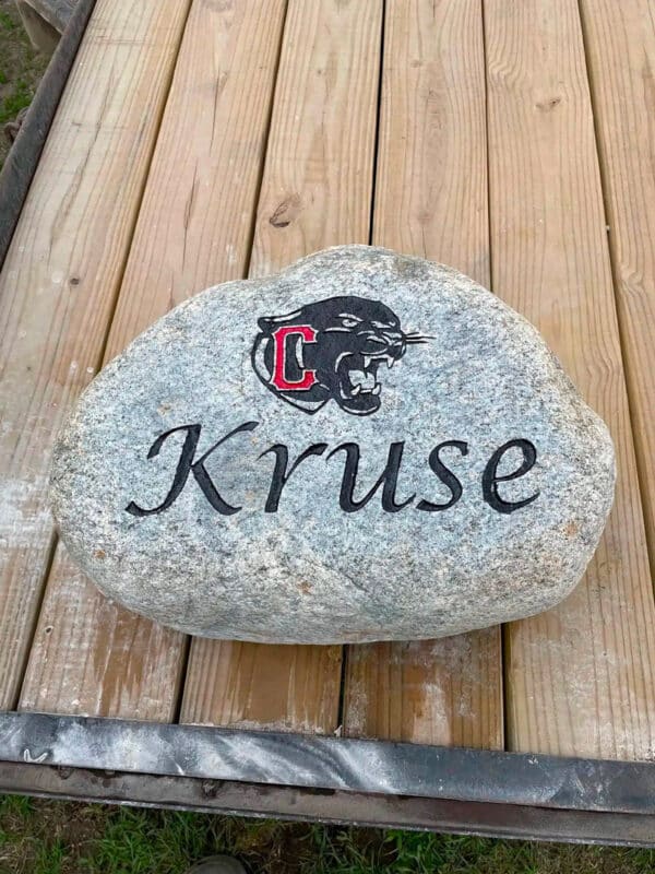 Custom engraved rock that says Kruse with logo painted in red and black