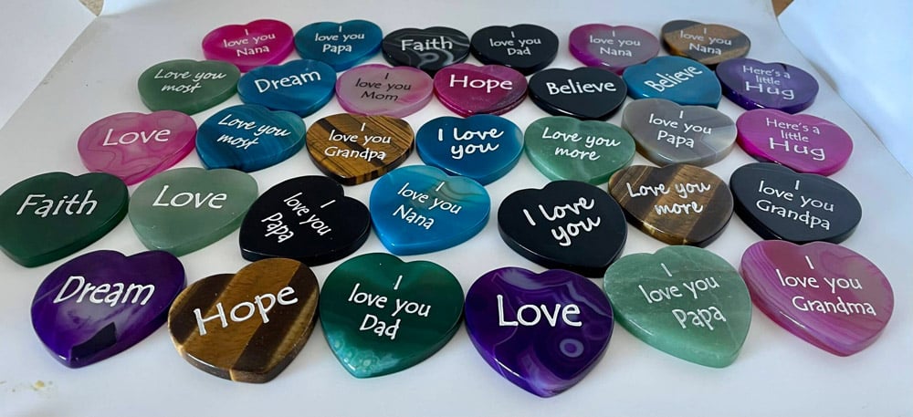 Heart shaped engraved stones in colors pink, blue, green, black, purple, and white. Most engraved with I love you.