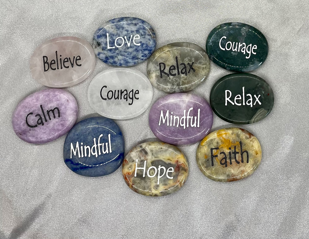 Round shaped engraved worry stones in colors pink, blue, green, yellow, purple, and white. Engraved with words like Relax, Calm, Courage, hope.