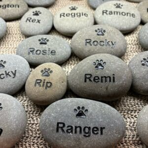 Multiple pet stones are shown with engraved paw prints and engraved pet names.