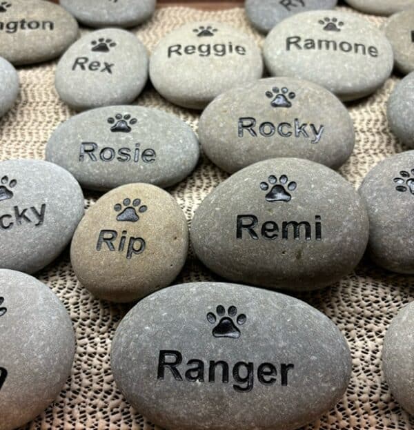 Multiple pet stones are shown with engraved paw prints and engraved pet names.