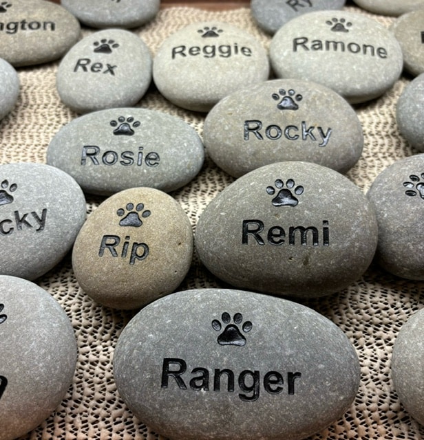 Multiple pet stones are shown with engraved paw prints and engraved pet names.